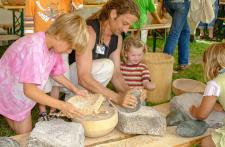  Museumsbesucher im Pfahlbaumuseum beim Getreide mahlen mit einem steinzeitlichen Mahlstein / Copyright: Pfahlbaumuseum Unteruhldingen