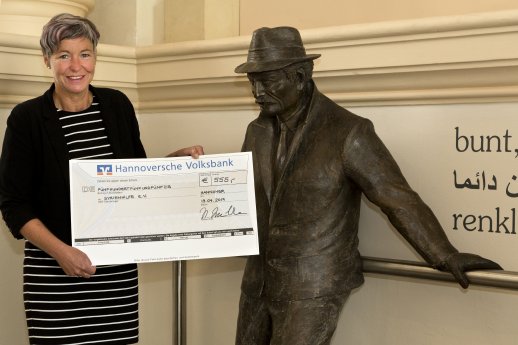 Katja Lembke mit Spendenscheck neben Statue Der Ausländer von Guido Messer (c) Landesmuseum Hann.jpg