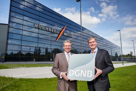 Platin-Gütesiegel in Sachen Nachhaltigkeit: Das Foto zeigt die beiden CEOs der NürnbergMesse, Roland Fleck und Peter Ottmann (von links), mit dem Platin-Zertifikat der Deutschen Gesellschaft für Nachhaltiges Bauen vor der neuen, 70 Millionen Euro teuren Messehalle 3C. Foto: obx-news/NürnbergMesse