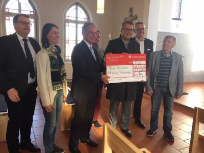 Landrat Ulrich Krebs und Markus Franz, Vorstandsmitglied der Taunus Sparkasse (2.v.r.), übergeben den Spendenscheck an die Vertreterinnen und Vertreter der Kirchengemeinde