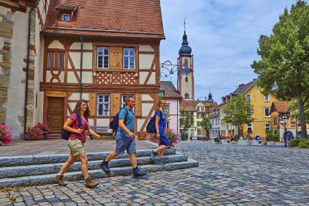 Wanderer auf dem LTM5 „Kirchen und Kleindenkmale“ am Schlossplatz in Tauberbischofsheim. Im Hintergrund der Turm der Stadtkirche St. Martin. Foto: Tourismusverband Liebliches Taubertal / Peter Frischmuth