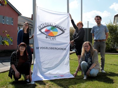 Die ehrenamtliche Beauftragte für Integration und Gleichstellung, Elisabeth Hillebrand (hinten, Zweite von rechts), die WIR-Koordinatorinnen Sonja Hartmann (hinten links) und Antonia Schäfer (vorne links) sowie die Koordinatorin des Familienbündnisses, Sandra Obenhack (rechts, vorne), hissen gemeinsam mit Simon Päbler, Sachgebietsleiter Sozialer Dienst sowie Koordinator und Sprecher des Familienbündnisses, die Fahne zur Interkulturellen Woche / Foto: Vogelsbergkreis/C.Lips