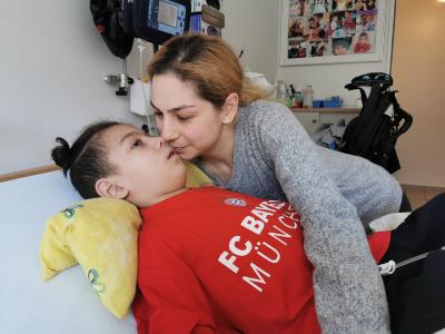 Ein Junge liegt mit offenen Augen im Bett. Seine Mutter beugt sich über sein Gesicht.