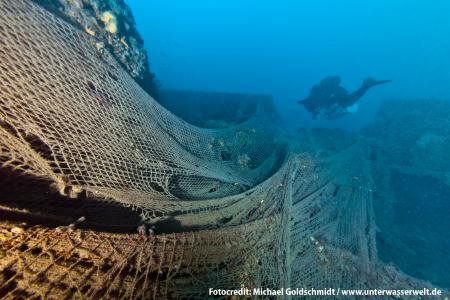 Taucher an einem Schiffswrack mit Geisternetzen