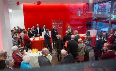 Landrat Ulrich Krebs (Bildmitte), Frederik Zölls, Marktbereichsleiter der Taunus Sparkasse im Hochtaunuskreis (rechts mit Mikrophon), und Thomas Blasini (links) begrüßten die knapp 130 Gäste, die zur Filialeröffnung gekommen waren