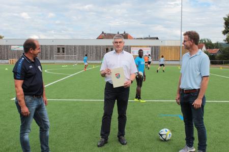 Mit knapp 4500 Euro aus Mitteln der Sportförderung unterstützt der Vogelsbergkreis den Jugendförderverein (JFV) Alsfeld, der auf dem Lindensportplatz einen neuen Kunstrasen hat auslegen lassen. Den entsprechenden Bescheid übergibt Landrat Manfred Görig Vorsitzendem Carsten Weitzel (links) und Vorstandsmitglied Jens Luckhard (rechts) / Foto: Sabine Galle-Schäfer/Vogelsbergkreis