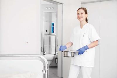 Pflegefachkraft trägt sauberes Steckbecken von der Patiententoilette ins Patientenzimmer