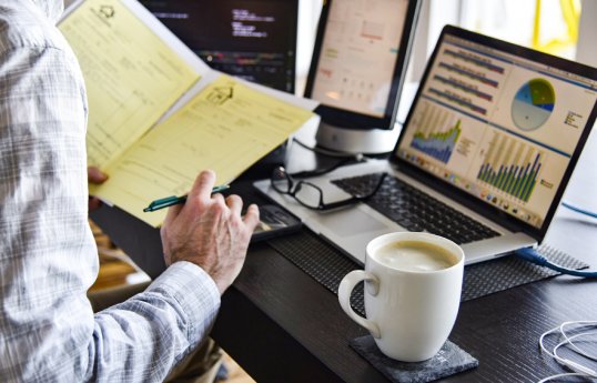 professional-at-desk-with-many-computers-signing-printed-contract-documents-coffee-charts-and-gr.jpg