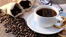 Kaffeetasse mit Kaffeebohnen steht auf Tisch