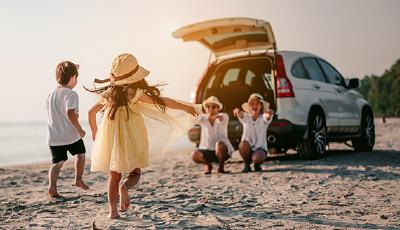 Familie am Strand vor Auto mit geöffneter Heckklappe
