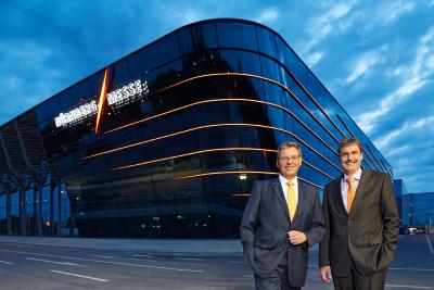 Blicken optimistisch in die Zukunft: die beiden CEOs der NürnbergMesse Group, Dr. Roland Fleck und Peter Ottmann, vor der Halle 3A. Sie entstand nach Plänen der berühmten Architektin Zaha Hadid. Auch die Halle 3C, die die Messe 2018 eröffnet, trägt die gestalterische Handschrift der Stararchitektin. Foto: obx-news/NürnbergMesse