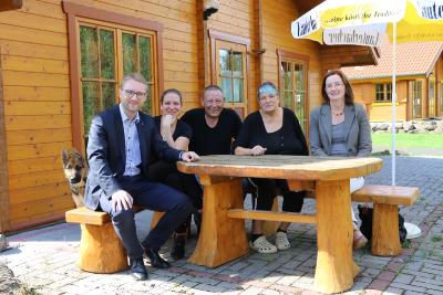 Im Gespräch vor einem Blockhaus der Pension „Grünes Paradies“ in Hochwaldhausen (v. l.): Wirtschaftsdezernent Dr. Jens Mischak, Diana, Armin und Christiane Dietrich sowie Andrea Ortstadt (Wirtschaftsförderung Vogelsbergkreis). Ganz links Schäferhundwelpe Ossi, der auch mit aufs Bild wollte (Foto: Gaby Richter)