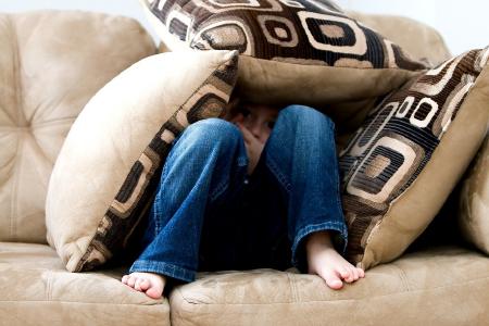 Kind auf der Couch unter Kissen versteckt. Foto: ambermb