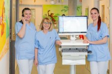 Das Bild zeigt drei Pflegefachkräfte, die den modernen Visitenwagen verwenden.